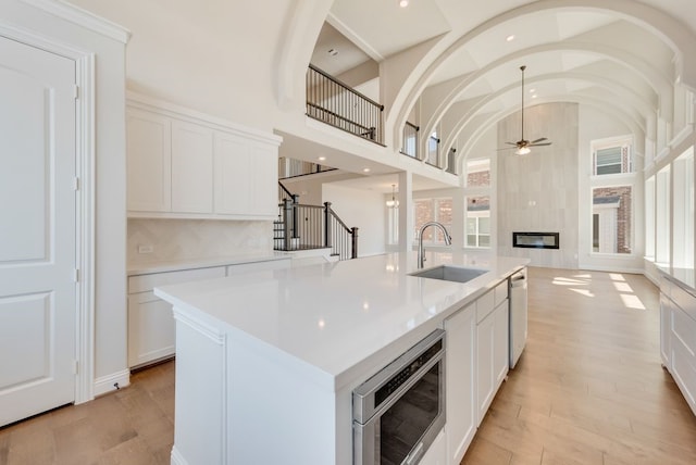 kitchen with light wood finished floors, ceiling fan, stainless steel microwave, and a sink