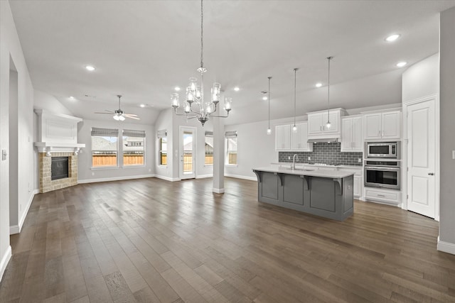 kitchen with white cabinetry, open floor plan, light countertops, appliances with stainless steel finishes, and a glass covered fireplace