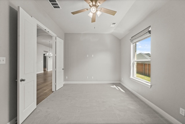 carpeted empty room with baseboards, visible vents, vaulted ceiling, and a ceiling fan