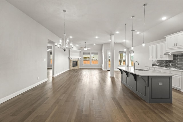 kitchen with decorative backsplash, open floor plan, a kitchen island with sink, white cabinetry, and a sink