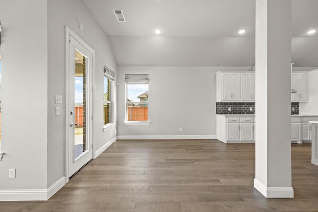 unfurnished dining area with light wood-style floors, visible vents, vaulted ceiling, and baseboards