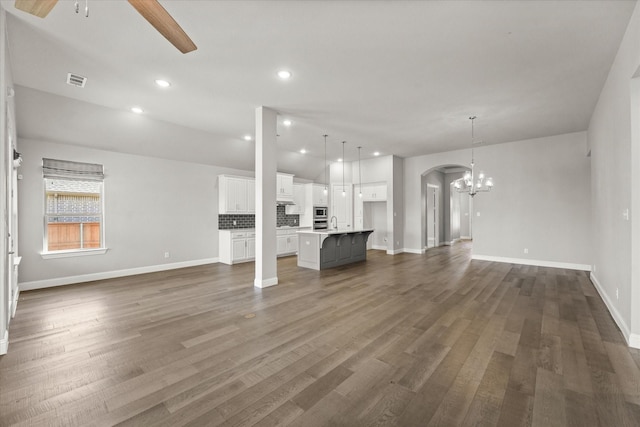 unfurnished living room with visible vents, arched walkways, dark wood-style floors, ceiling fan with notable chandelier, and recessed lighting