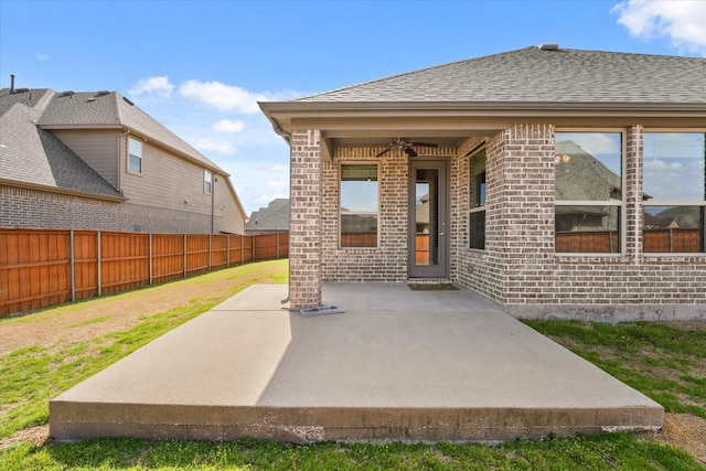 doorway to property with brick siding, roof with shingles, a ceiling fan, a patio area, and fence