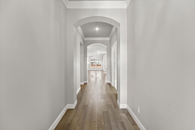 corridor featuring ornamental molding, arched walkways, dark wood-style flooring, and baseboards