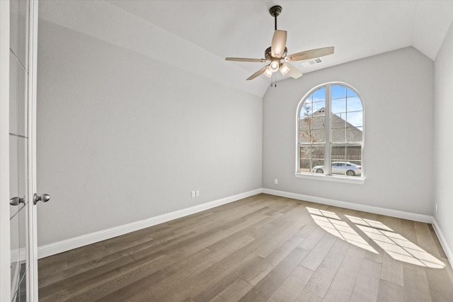 spare room with lofted ceiling, wood finished floors, visible vents, and baseboards