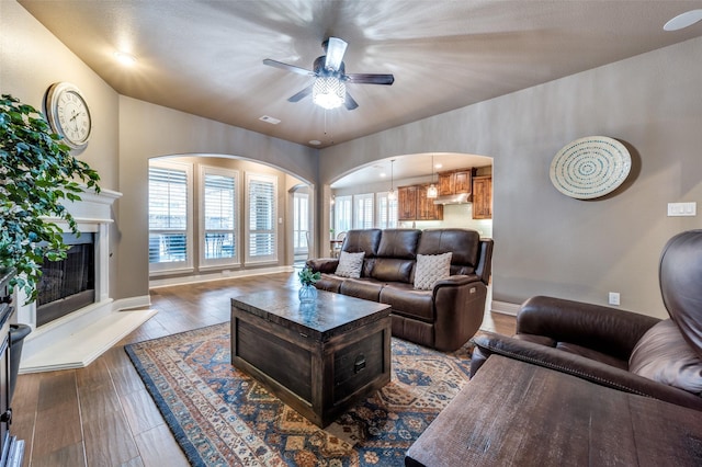 living room featuring wood finished floors, baseboards, visible vents, a fireplace with raised hearth, and ceiling fan