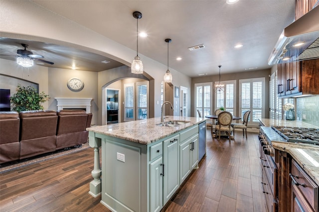 kitchen with visible vents, a sink, open floor plan, wall chimney range hood, and dishwasher