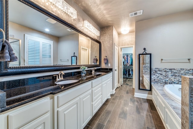 bathroom featuring visible vents, a walk in closet, double vanity, a bath, and a sink