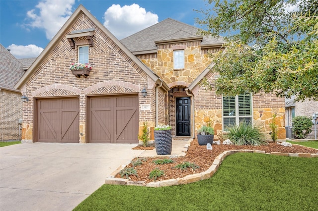 view of front of house featuring driveway, an attached garage, a shingled roof, stone siding, and brick siding