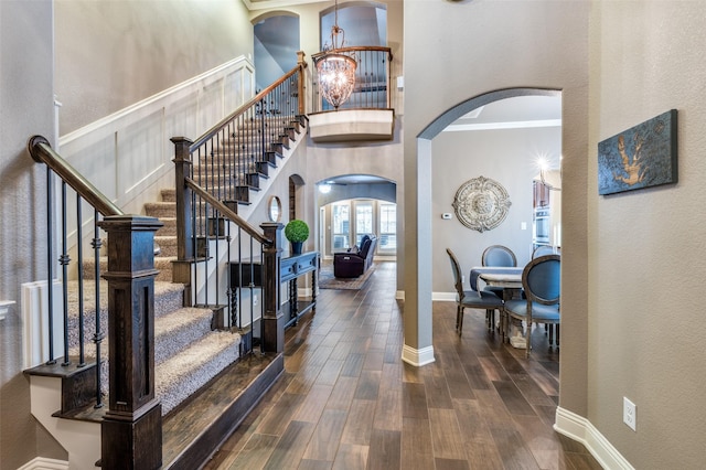 entryway with baseboards, a high ceiling, an inviting chandelier, wood finished floors, and arched walkways