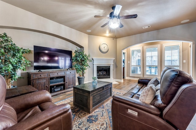 living area featuring visible vents, a fireplace with raised hearth, baseboards, wood finished floors, and a ceiling fan