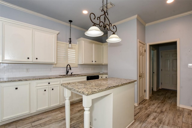 kitchen with light wood finished floors, tasteful backsplash, ornamental molding, pendant lighting, and a sink