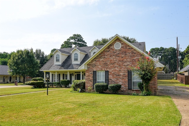 cape cod house with brick siding, fence, a front lawn, and roof with shingles