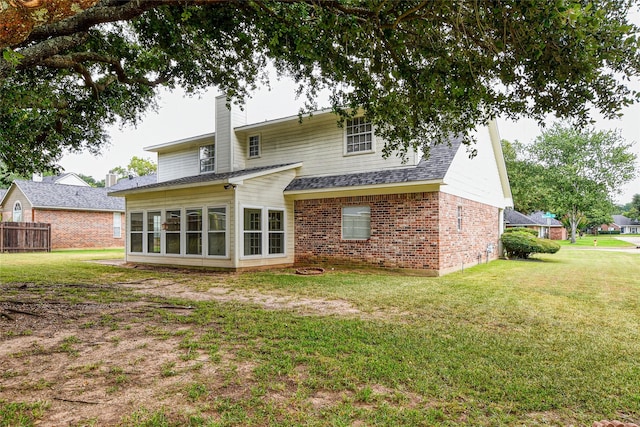 rear view of property featuring brick siding, a chimney, a shingled roof, a lawn, and fence