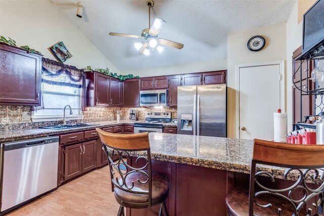 kitchen with decorative backsplash, dark countertops, lofted ceiling, appliances with stainless steel finishes, and a breakfast bar area