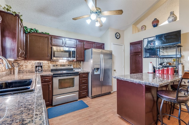 kitchen featuring light wood finished floors, backsplash, appliances with stainless steel finishes, vaulted ceiling, and a sink