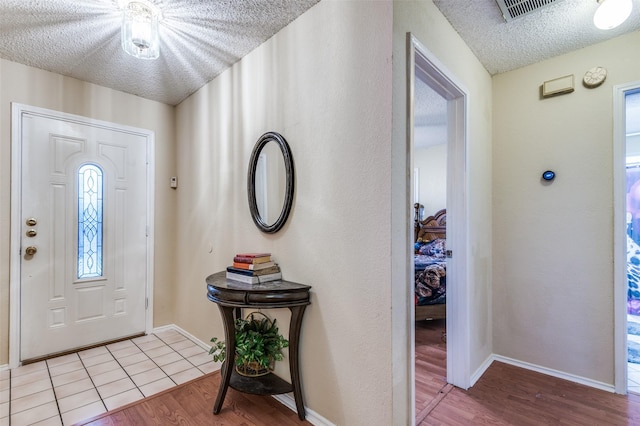 foyer with light wood-type flooring, visible vents, a textured ceiling, and baseboards