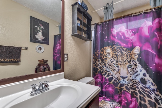 full bathroom featuring toilet, a textured wall, a textured ceiling, and vanity