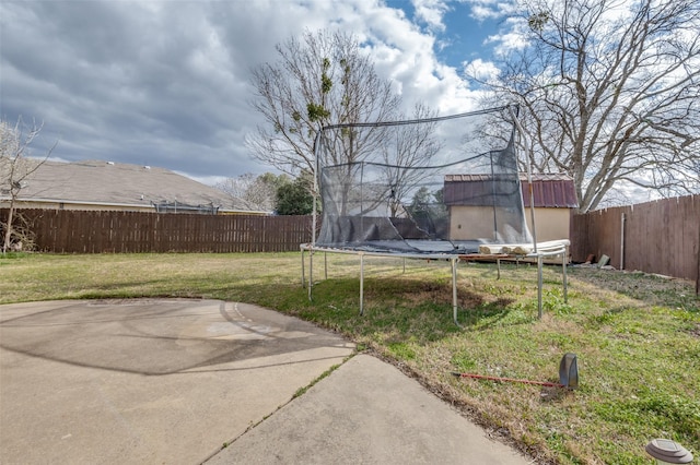 view of yard featuring a trampoline, a fenced backyard, a patio, and an outdoor structure