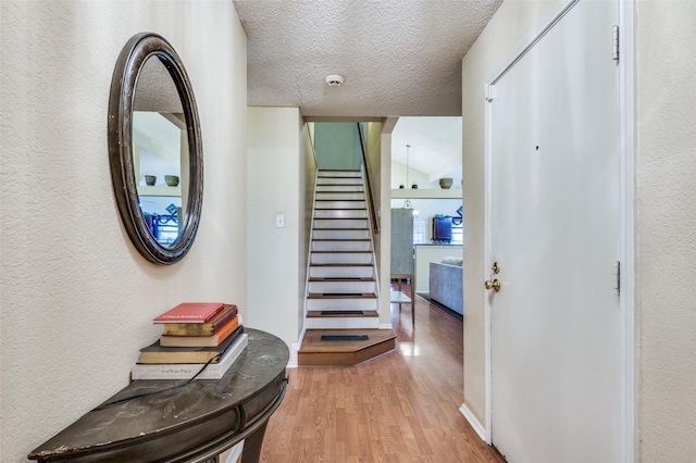 corridor featuring baseboards, a textured wall, stairway, wood finished floors, and a textured ceiling