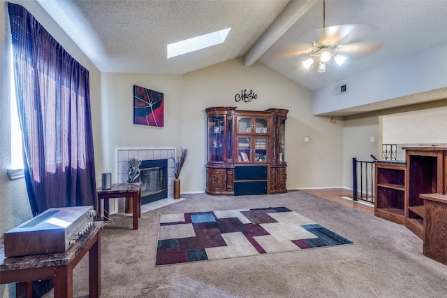 carpeted living room featuring ceiling fan, a textured ceiling, a tile fireplace, vaulted ceiling with skylight, and baseboards