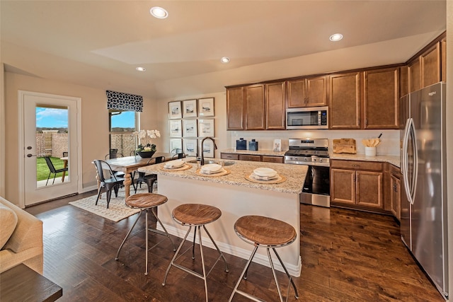 kitchen with a sink, a kitchen bar, appliances with stainless steel finishes, and dark wood finished floors