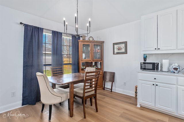 dining space with a chandelier, light wood finished floors, lofted ceiling, and baseboards