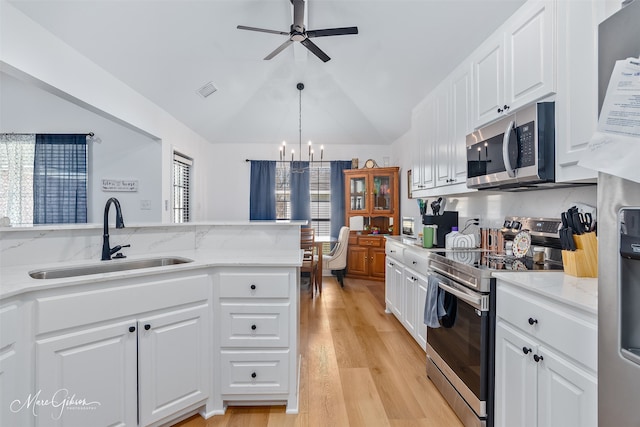 kitchen with lofted ceiling, light wood-style flooring, stainless steel appliances, white cabinetry, and a sink