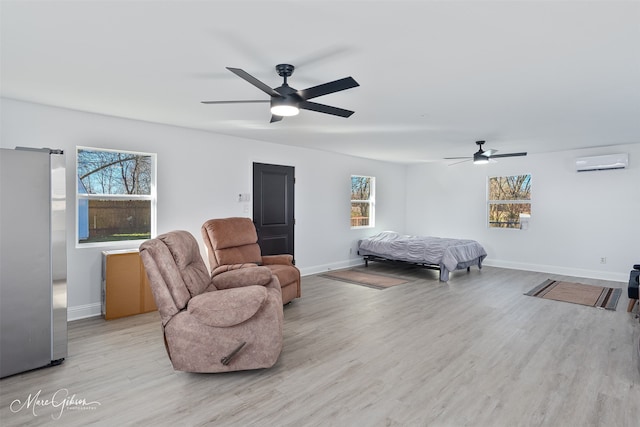 bedroom featuring light wood finished floors, baseboards, ceiling fan, freestanding refrigerator, and an AC wall unit