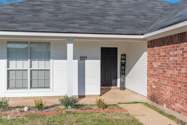 view of exterior entry featuring brick siding and roof with shingles