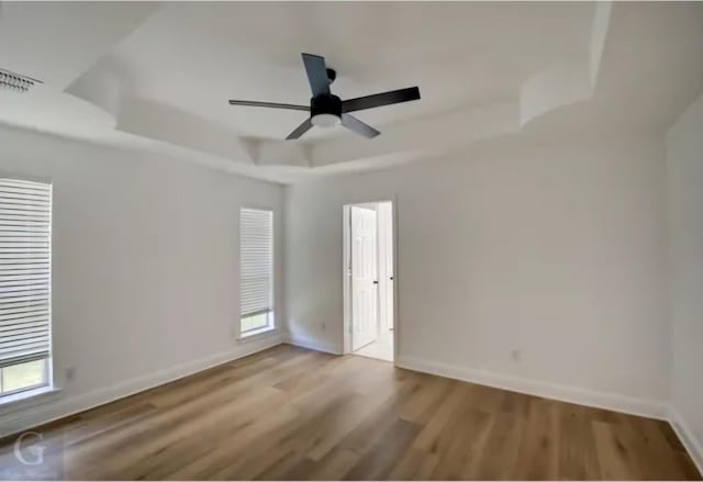 unfurnished room featuring wood finished floors, a raised ceiling, visible vents, and baseboards