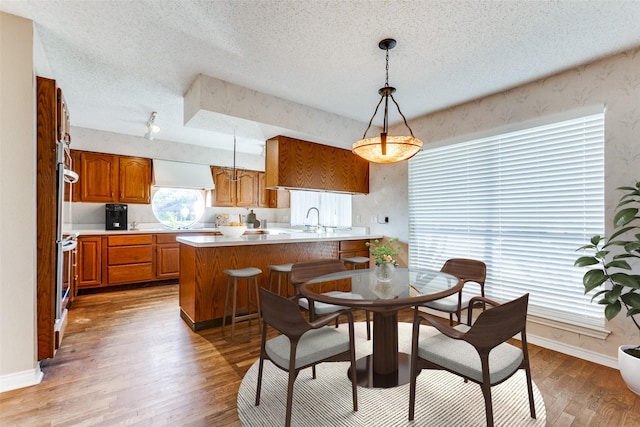 kitchen featuring a peninsula, a sink, light wood-type flooring, brown cabinets, and custom range hood