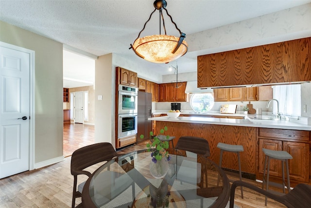 kitchen featuring brown cabinetry, a peninsula, light countertops, stainless steel double oven, and a sink