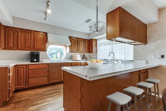 kitchen with brown cabinetry, a kitchen breakfast bar, custom exhaust hood, a textured ceiling, and light wood-type flooring