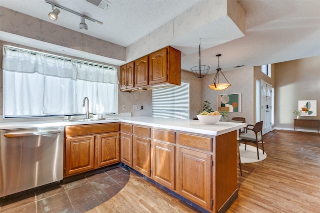 kitchen featuring a textured ceiling, a peninsula, a sink, brown cabinets, and dishwasher