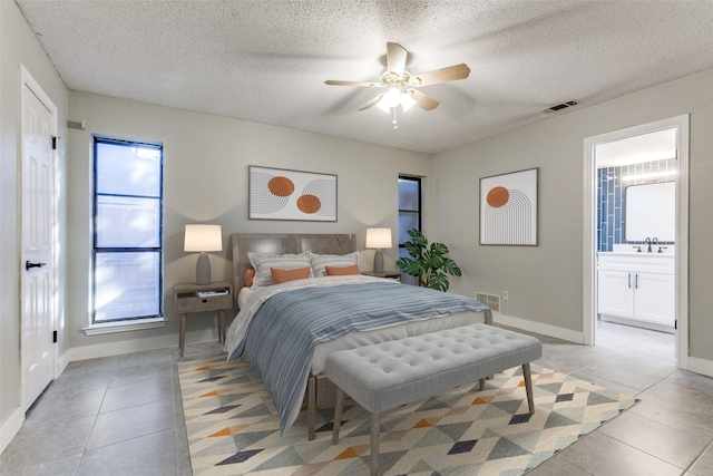 bedroom featuring a textured ceiling, light tile patterned flooring, a sink, visible vents, and ensuite bath