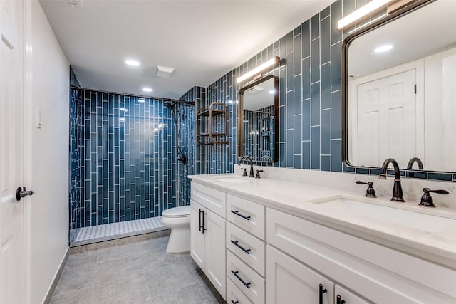 full bathroom featuring toilet, double vanity, a tile shower, and a sink