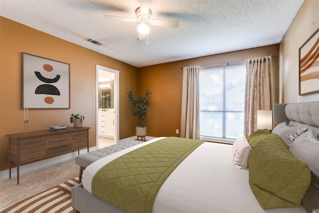 bedroom with light tile patterned floors, visible vents, a ceiling fan, ensuite bath, and a textured ceiling