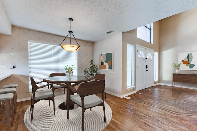 dining area with baseboards, wood finished floors, visible vents, and wallpapered walls