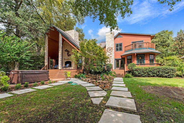 view of front of house with an outdoor stone fireplace, a hot tub, a balcony, stone siding, and a front lawn