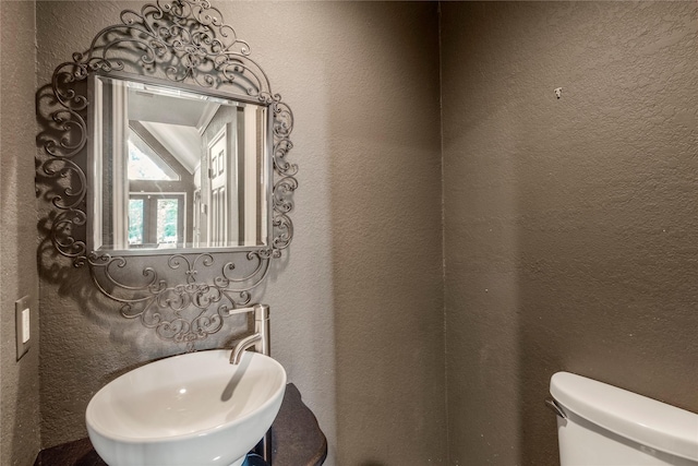 bathroom with toilet, a sink, and a textured wall