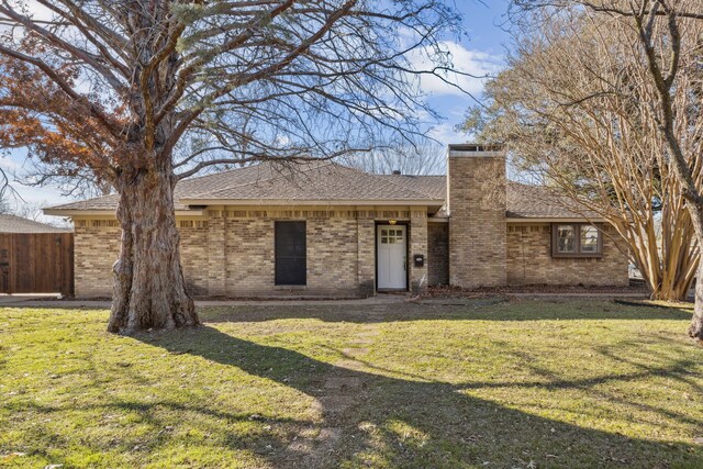 ranch-style house featuring brick siding, a chimney, fence, and a front yard