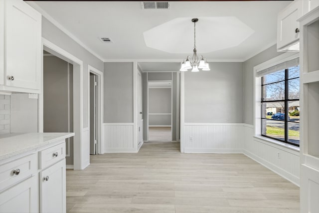 unfurnished dining area with a wainscoted wall, light wood-type flooring, and visible vents