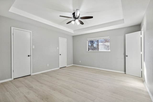 unfurnished bedroom featuring light wood finished floors, baseboards, a tray ceiling, and ceiling fan