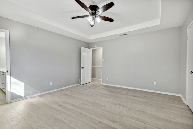 spare room featuring light wood-style flooring, visible vents, a raised ceiling, and baseboards