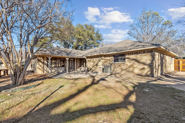 view of front of property featuring central AC, brick siding, a shingled roof, fence, and a front lawn