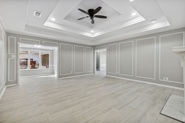 interior space with crown molding, a raised ceiling, visible vents, a decorative wall, and light wood-style floors