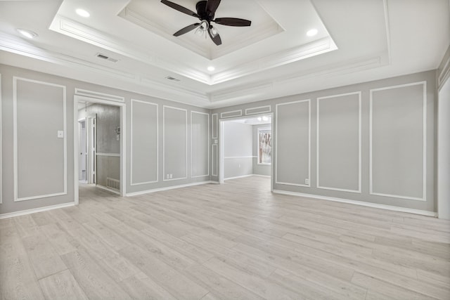 unfurnished bedroom with crown molding, light wood finished floors, a raised ceiling, visible vents, and a decorative wall