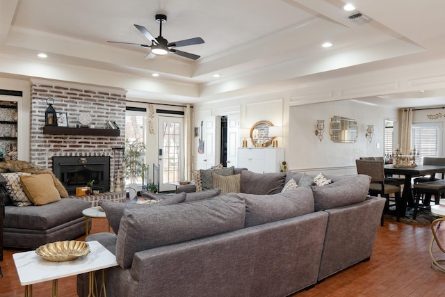 living room featuring a fireplace, wood finished floors, visible vents, a tray ceiling, and crown molding