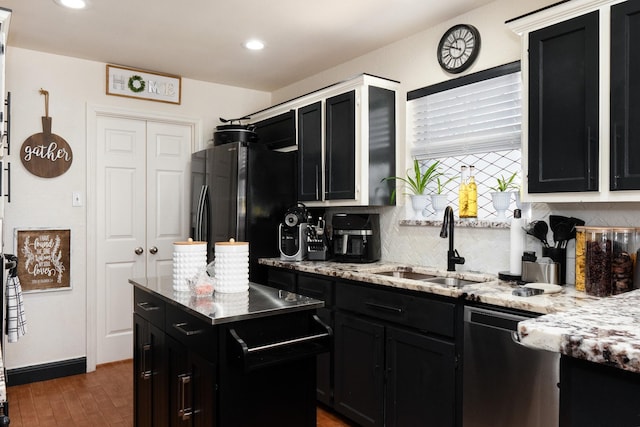 kitchen featuring a sink, dark cabinetry, backsplash, freestanding refrigerator, and dishwasher